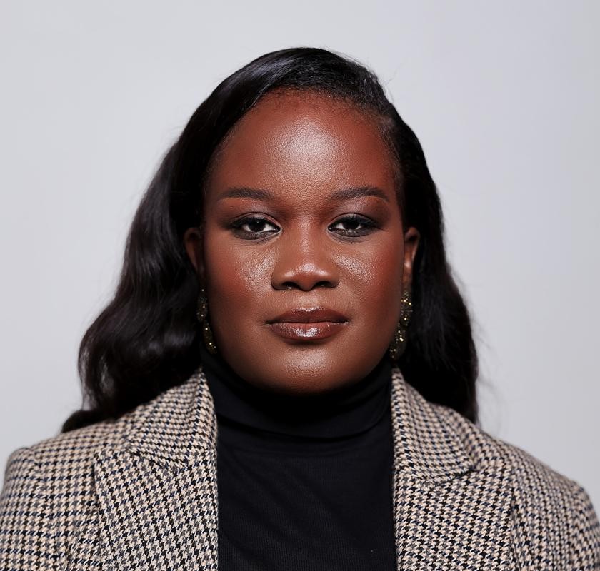 Portrait of female founder sitting at a conference table with laptop, late 30s, professional blazer, warm expression while holding a coffee cup